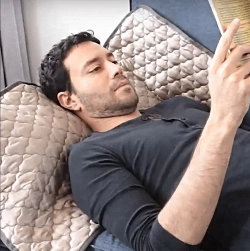 Joven relajado leyendo un libro sin estrés, recostado sobre una cobija Nikken que brinda confort y descanso profundo